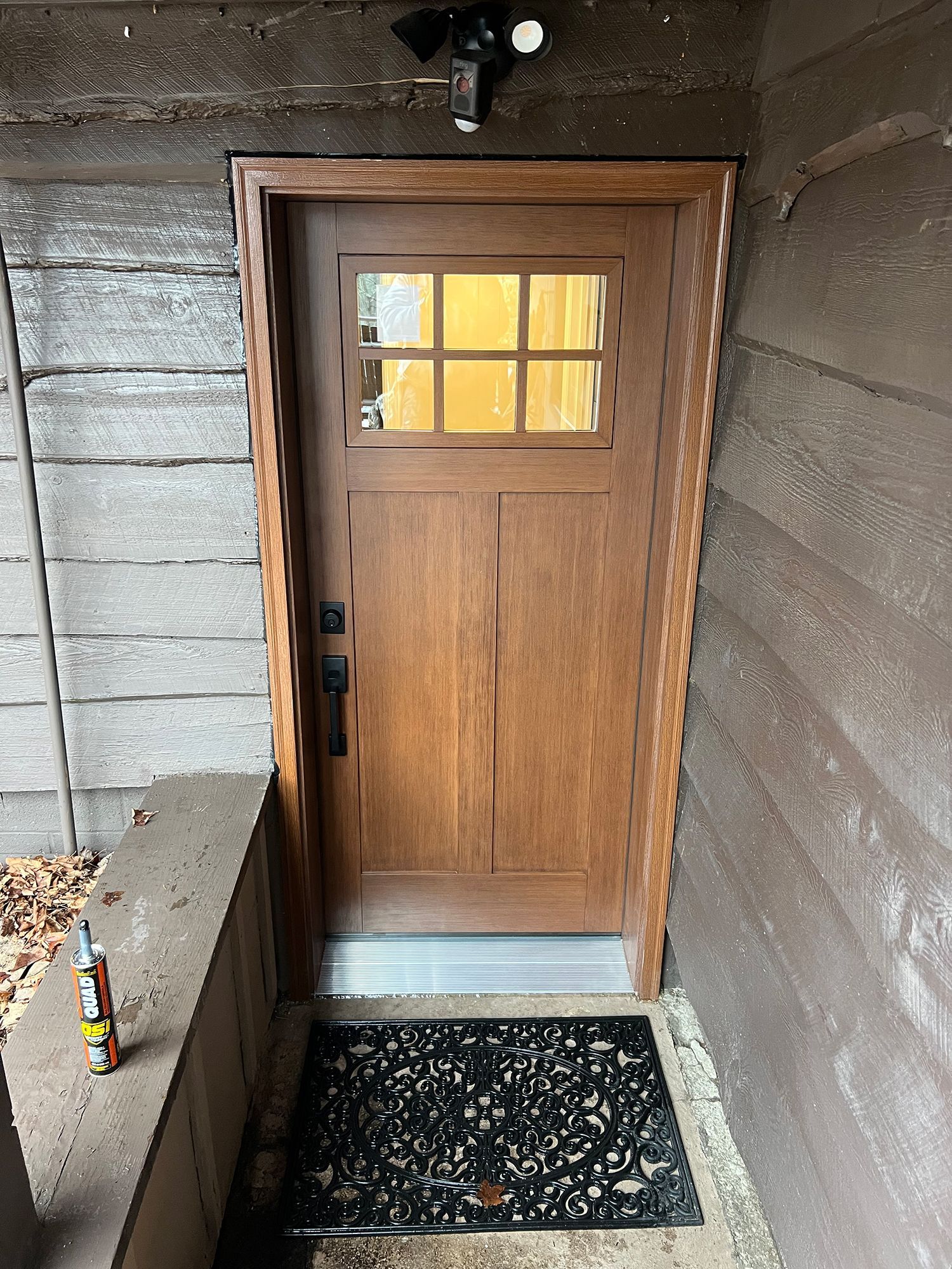 Wooden front door with glass window and security light.