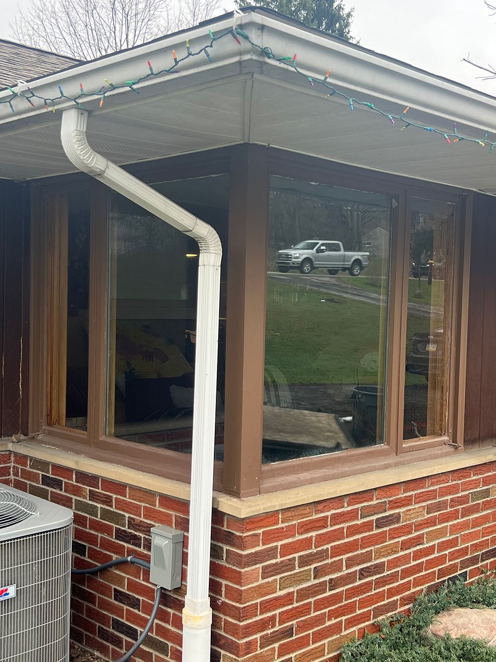 Corner of a brick house with large windows, white gutter, and an air conditioning unit. A truck is reflected in the glass.