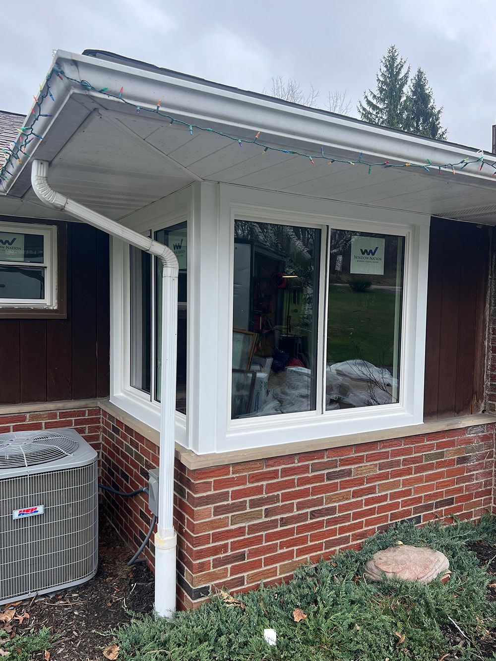 Bay window with white trim and white gutters on a brick house, with an AC unit.