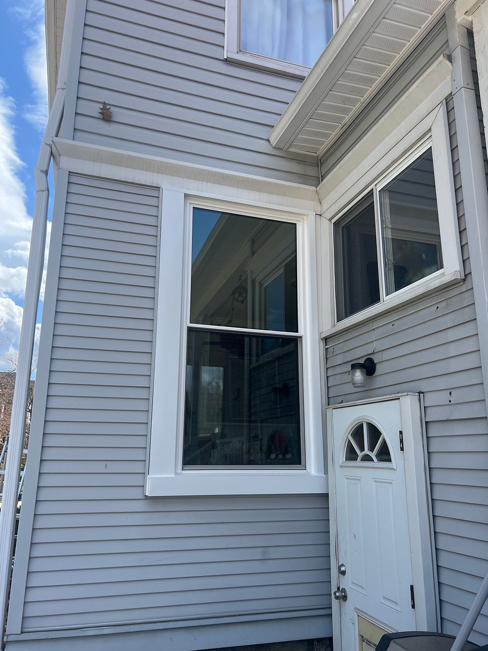 Exterior of a gray building with a large white-framed window and a white door. Blue sky visible.