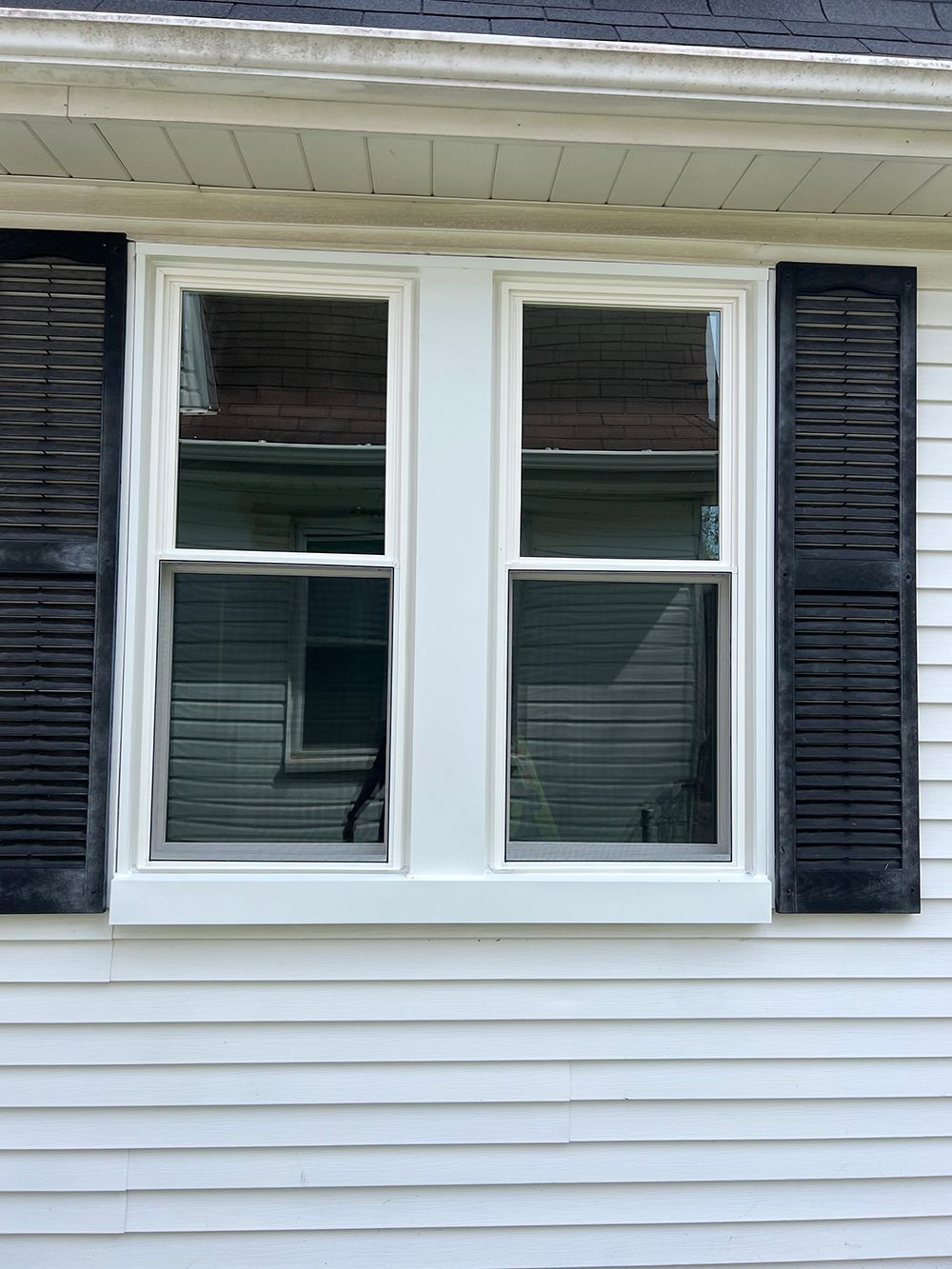 Two white-framed windows with black shutters on a white house.