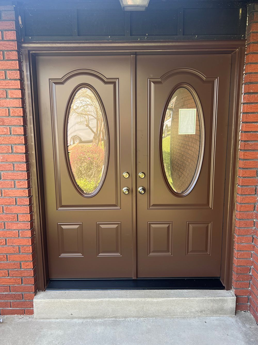 Brown double doors with oval windows and brick surroundings.