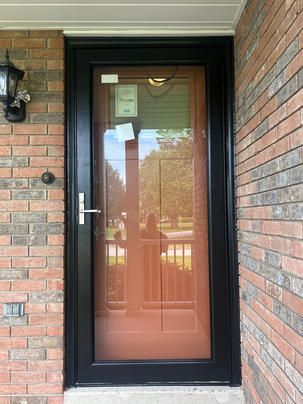 Black framed front door with bronze-tinted glass and a silver handle, set in a brick wall.