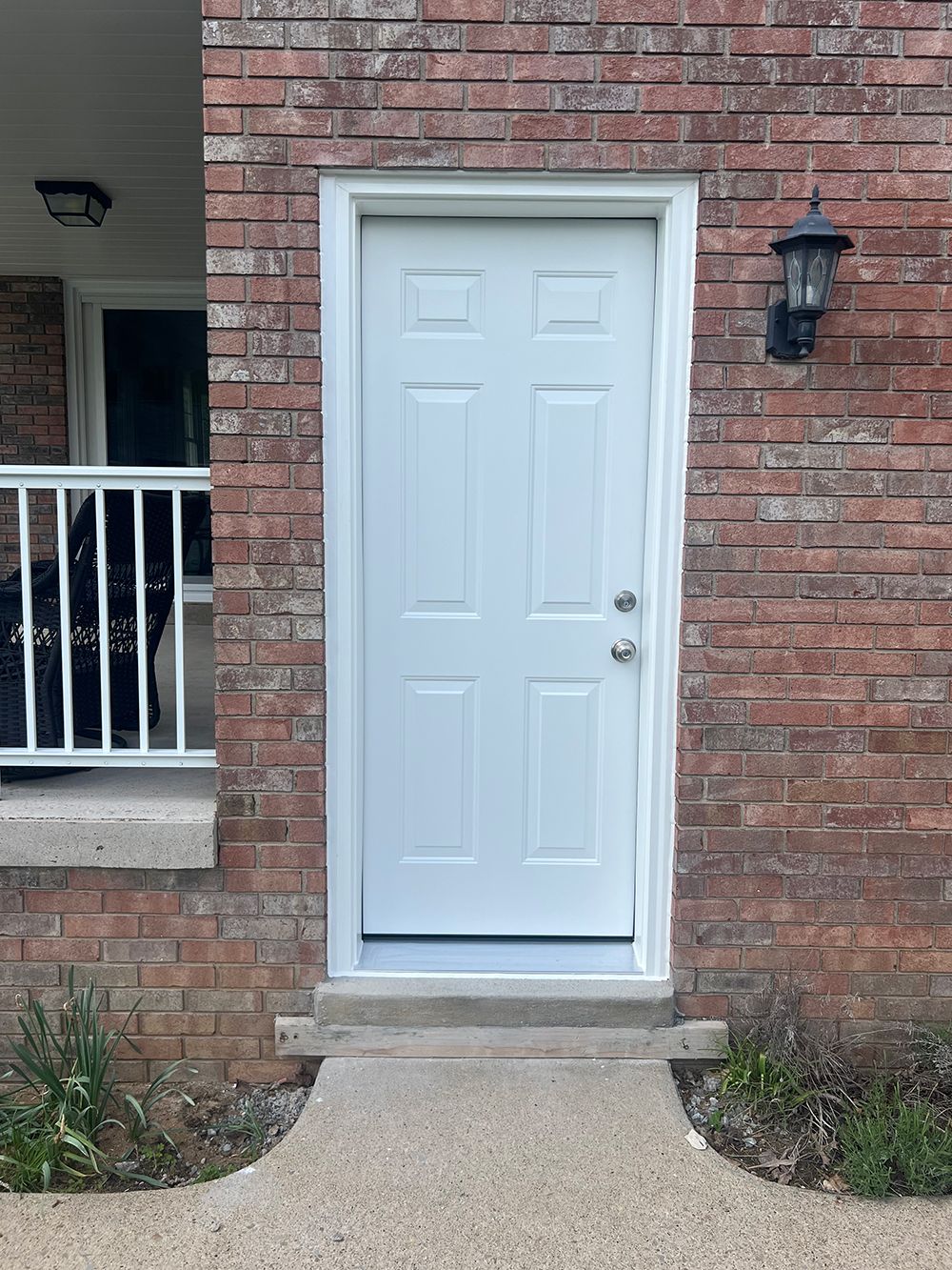 White door with white trim on a brick building with a concrete pathway.