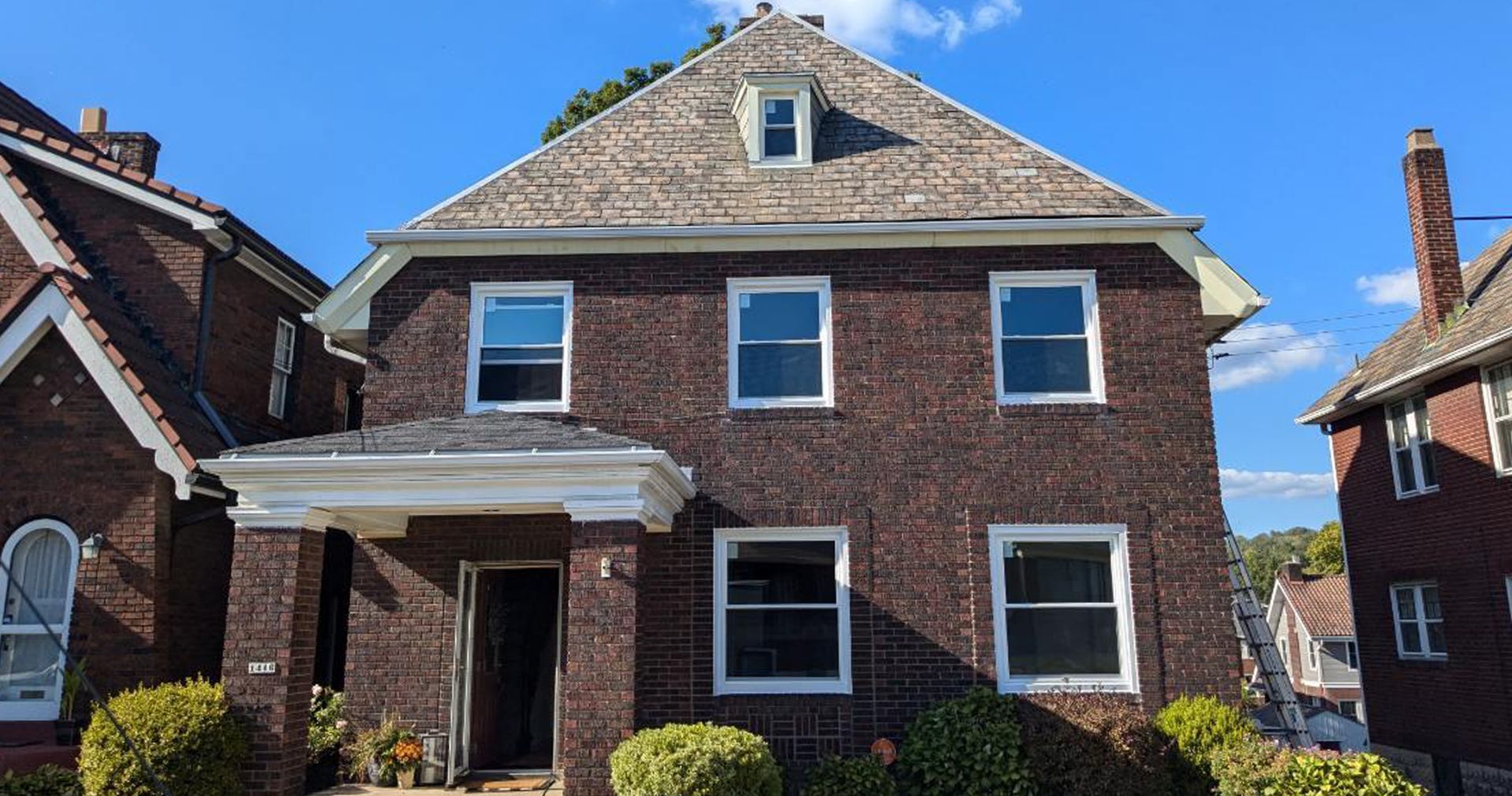 Two-story brick house with several windows and a gabled roof under a blue sky.