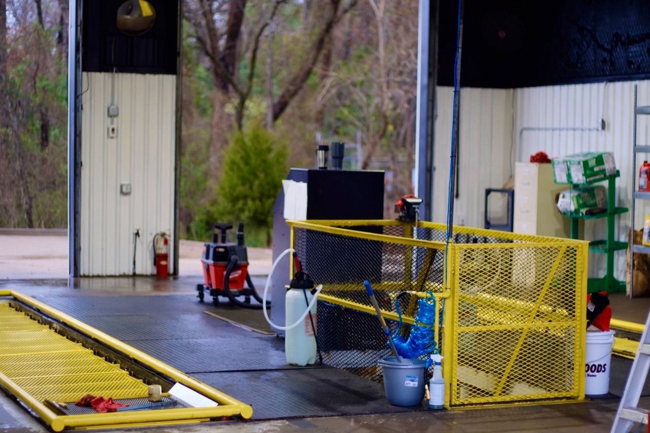 Open garage with yellow safety gates, tools, and machinery; rainy outdoor setting.