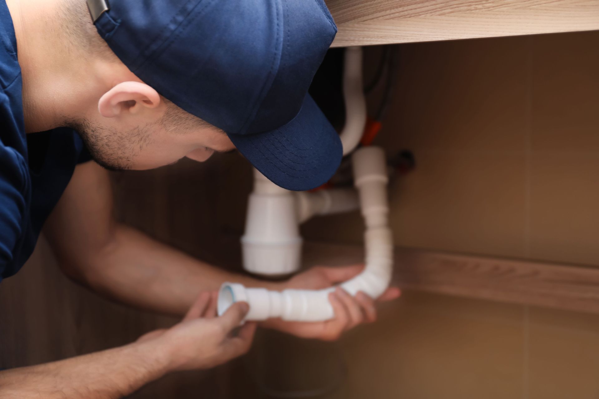 A man in a blue hat is fixing a sink pipe.