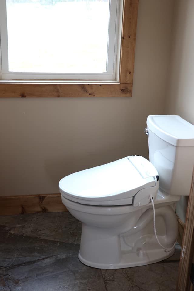 A white toilet is sitting in a bathroom next to a window.