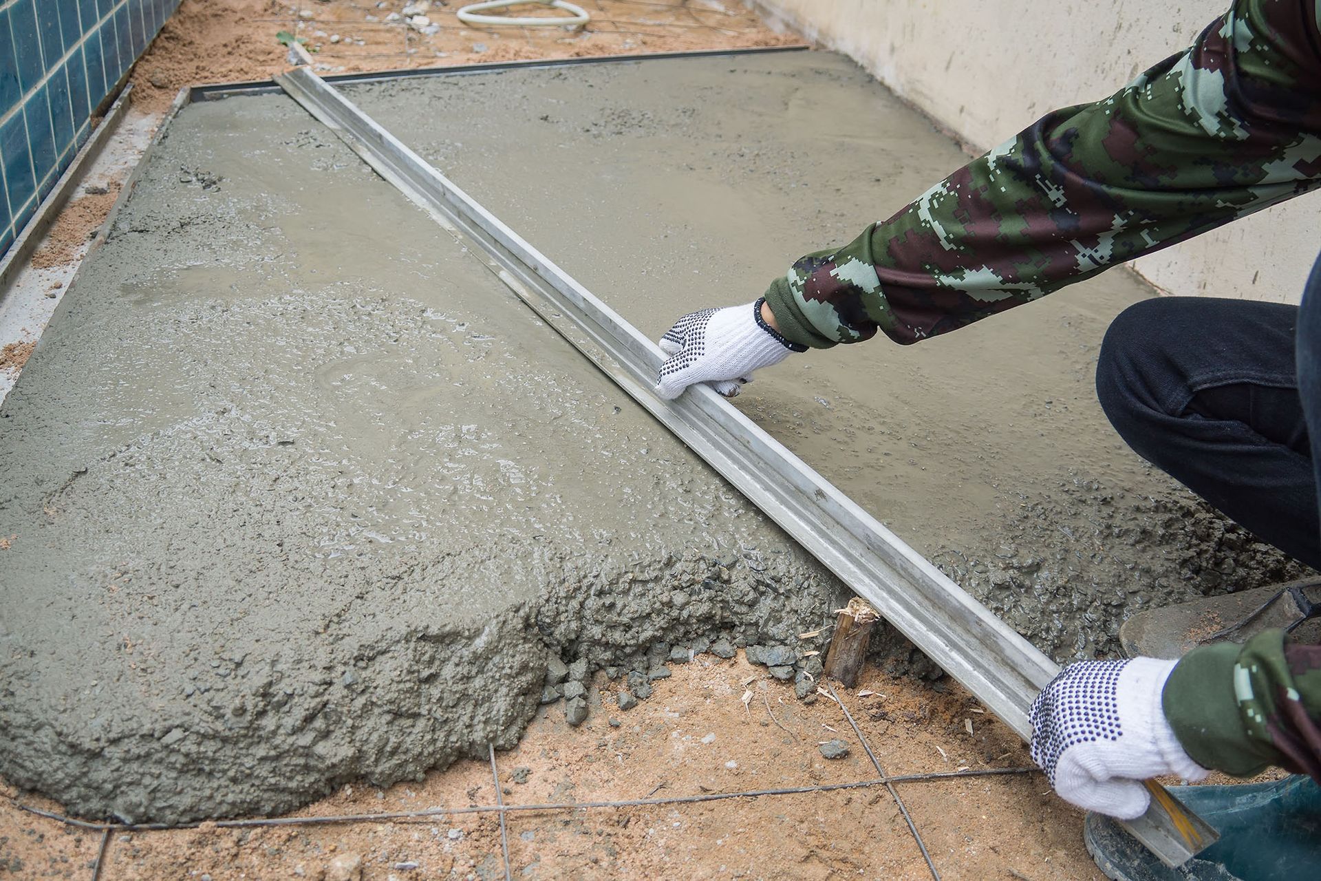 Worker smoothing fresh concrete with a straightedge in a narrow outdoor area