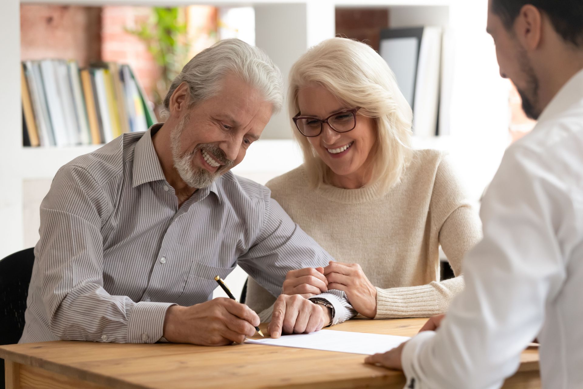Smiling elderly couple signing document at desk with advisor.