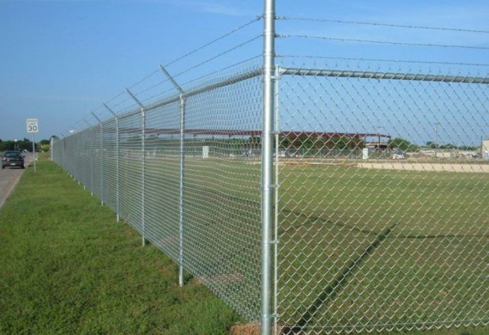 A chain link fence is surrounding a grassy field.