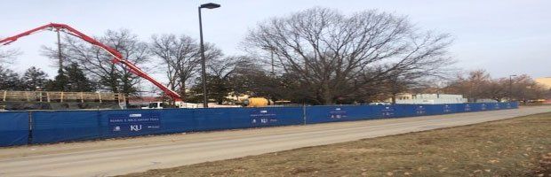 A roller coaster is being built in a park behind a blue fence.