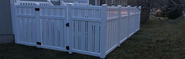 A white fence is sitting in the grass in front of a house.