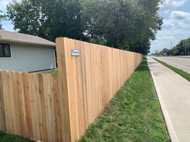 A wooden fence along the side of a road next to a house.