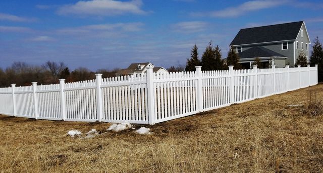 A white fence surrounds a grassy field in front of a house.
