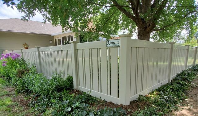 A white fence with a tree in the background is in front of a house.