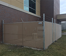 A chain link fence is sitting next to a brick building.