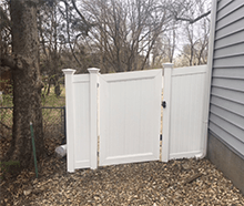 A white fence with a gate in the backyard of a house.