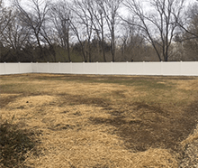 A large empty field with a white fence and trees in the background.