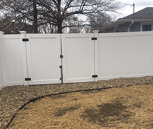 A white vinyl fence with a gate in the backyard of a house.