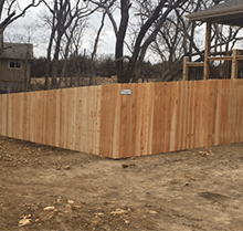 A wooden fence is sitting in the middle of a dirt field next to a house.