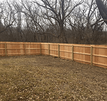 A wooden fence surrounds a lush green yard with trees in the background.
