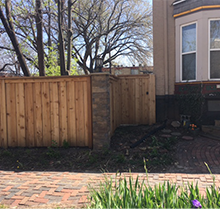 A wooden fence is surrounding a brick driveway in front of a house.