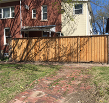 A wooden fence is surrounding a brick driveway in front of a house.