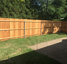 A wooden fence is sitting on top of a lush green lawn next to a sidewalk.