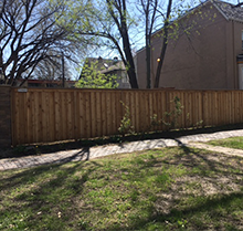 A wooden fence surrounds a lush green yard in front of a house.