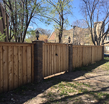A wooden fence with a gate in the middle of a driveway next to a house.