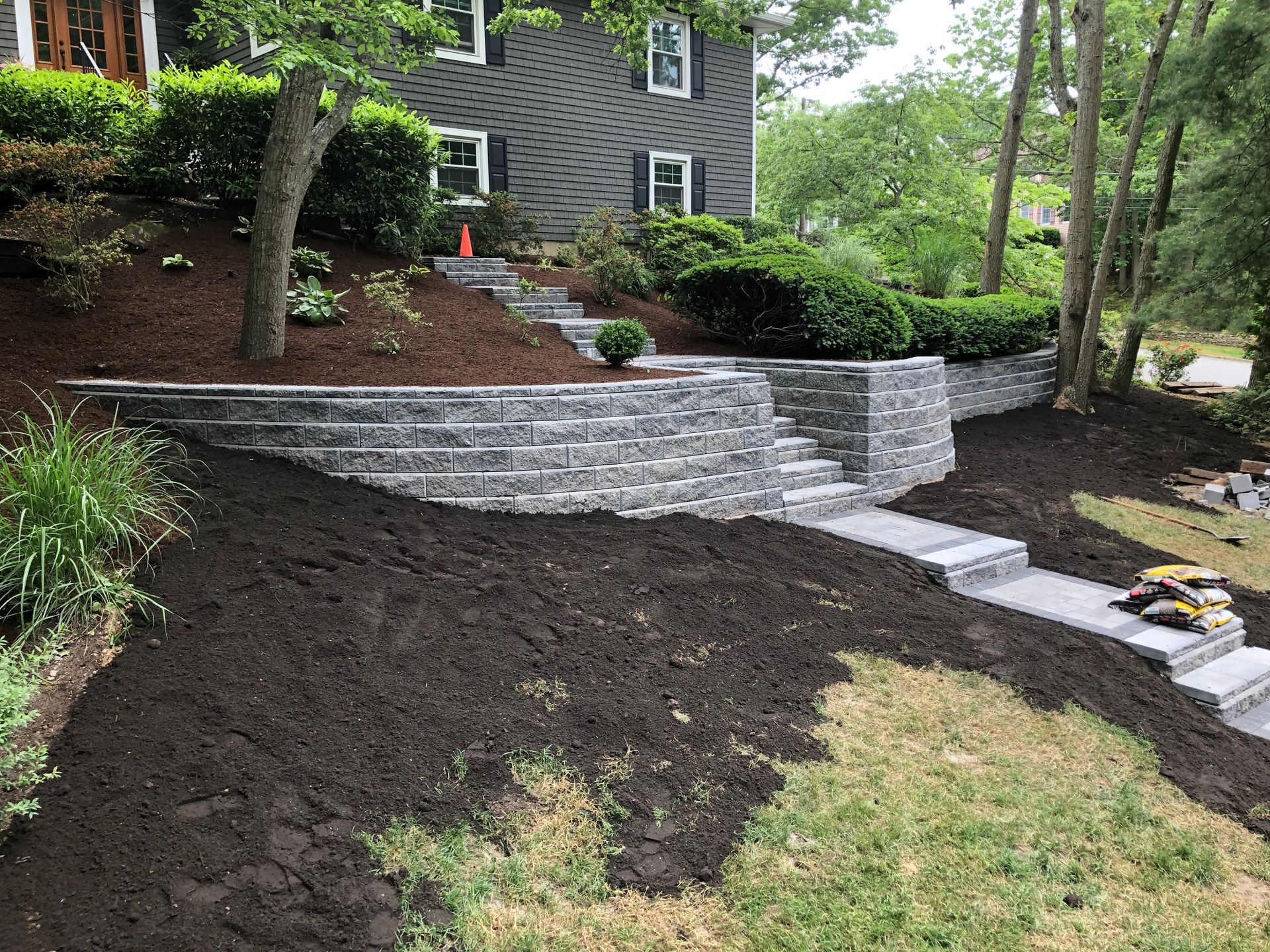 Stone steps and retaining walls lead up to a dark grey house with a landscaped yard.