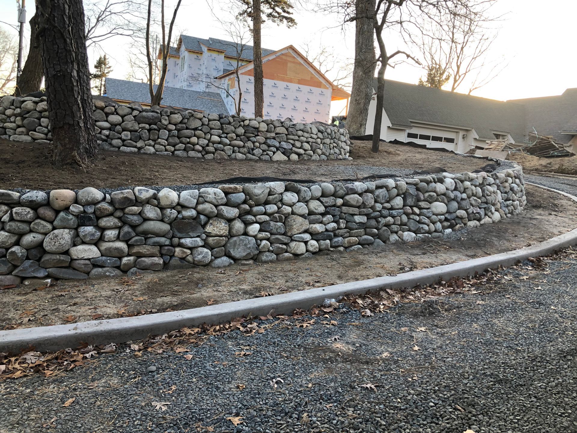 Stone retaining walls, gravel, and a house under construction.
