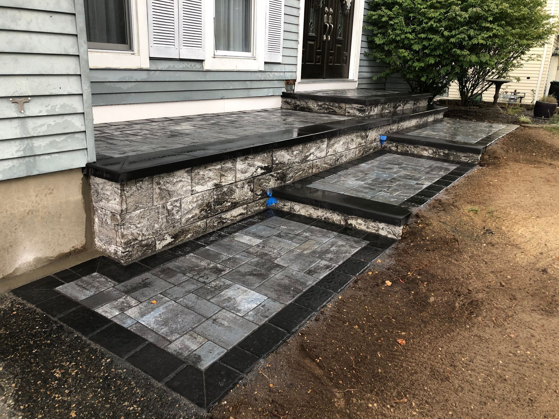 Stone steps with black borders leading to a house, with a grey facade and greenery.