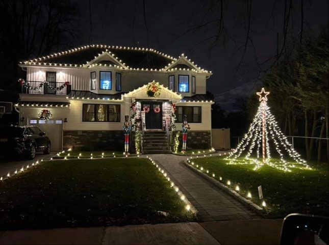 Lit-up two-story house at night with Christmas lights, lawn decorations, and a tree-shaped light display.