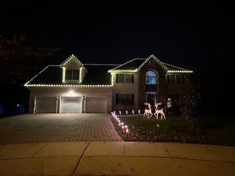 A house decorated with white Christmas lights, a brick facade, reindeer lawn ornaments, and path lighting.