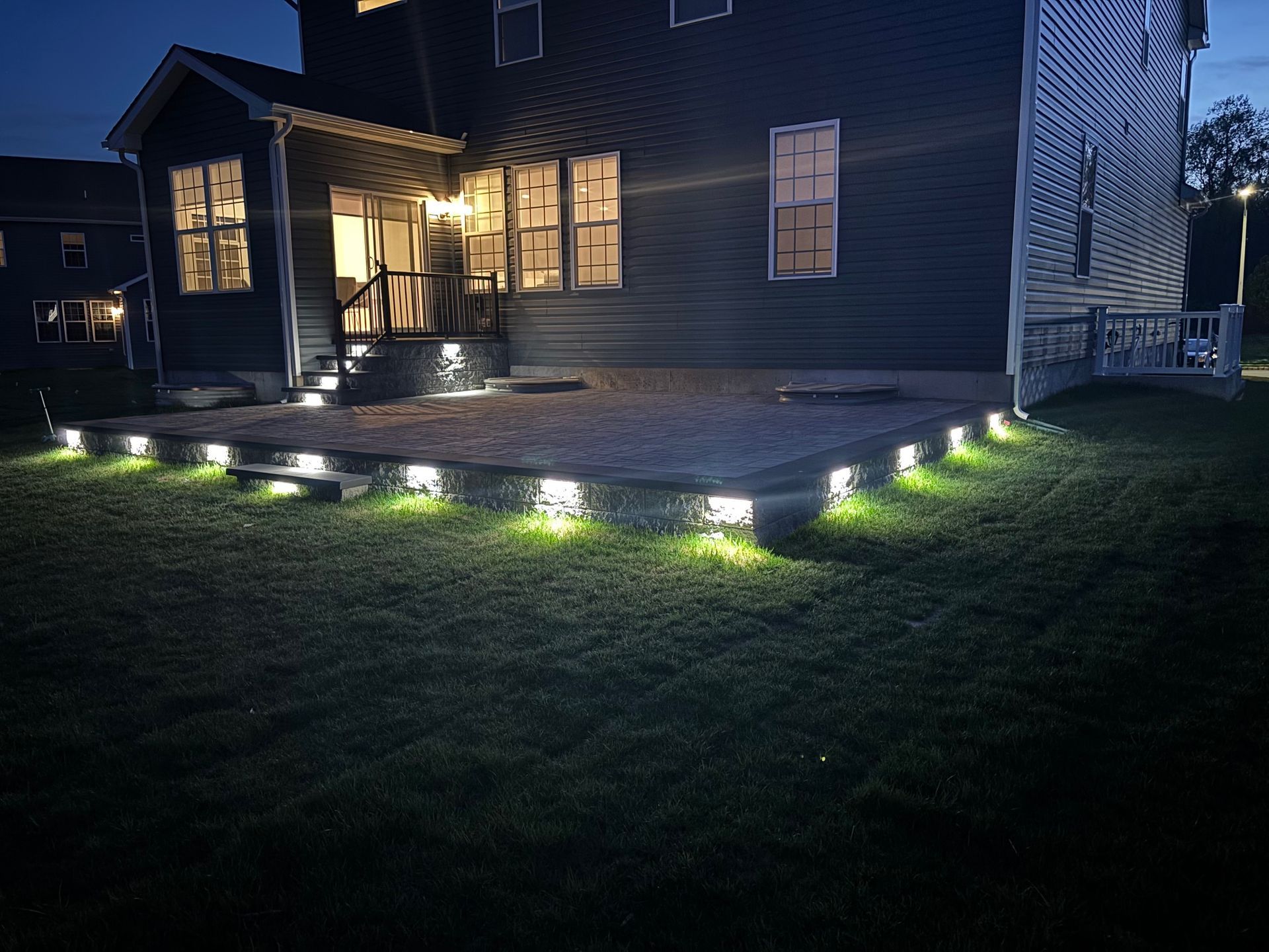 A house at night, lit patio, and lawn with ground lights.