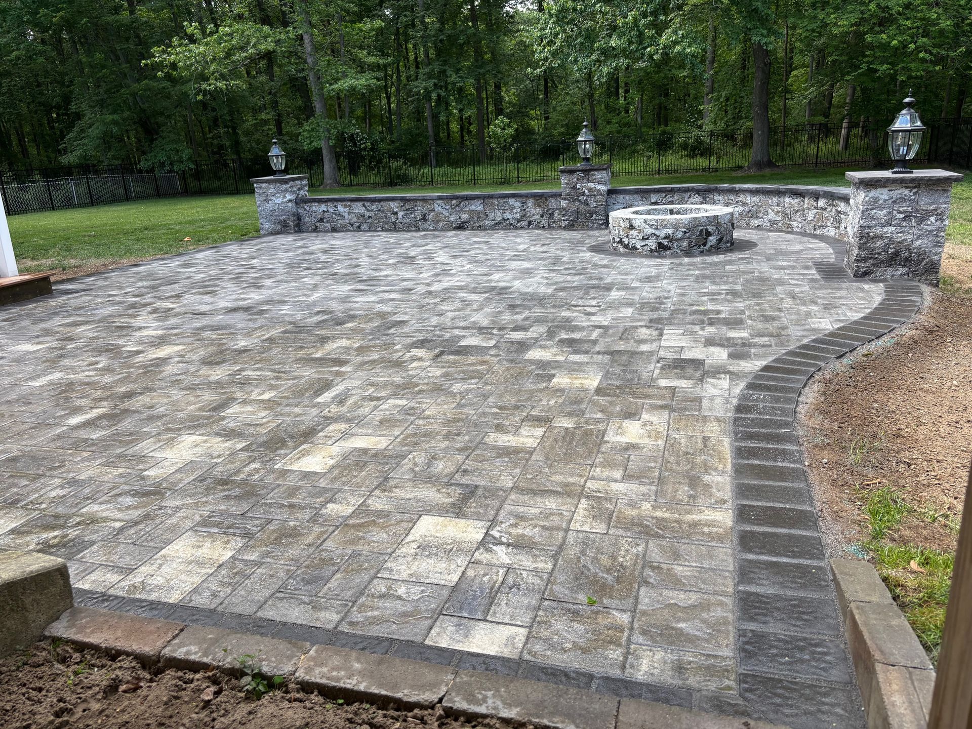 Stone patio with fire pit and decorative wall in a backyard.