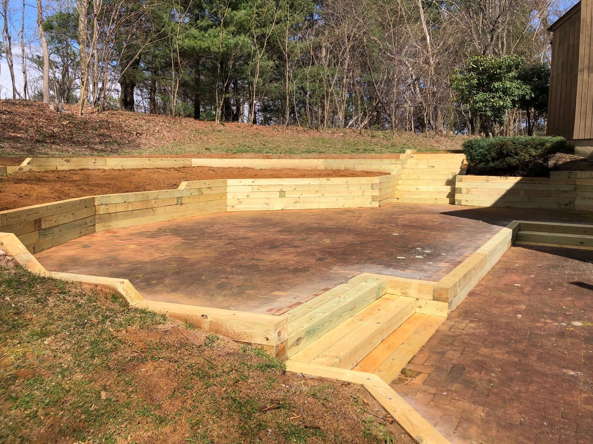 Wooden retaining walls create tiered outdoor space with steps. Earth and grass surround it.