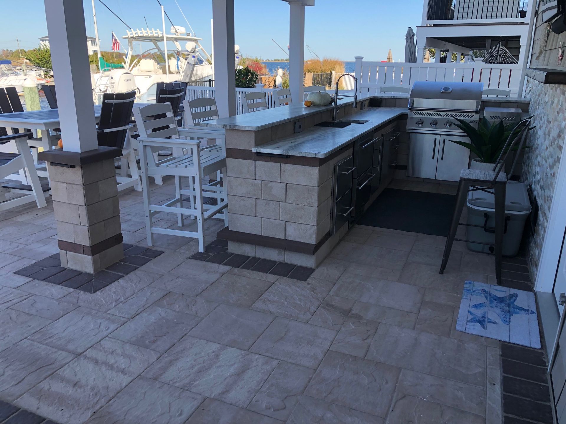 Outdoor kitchen with grill, counter, and bar stools on a patio.