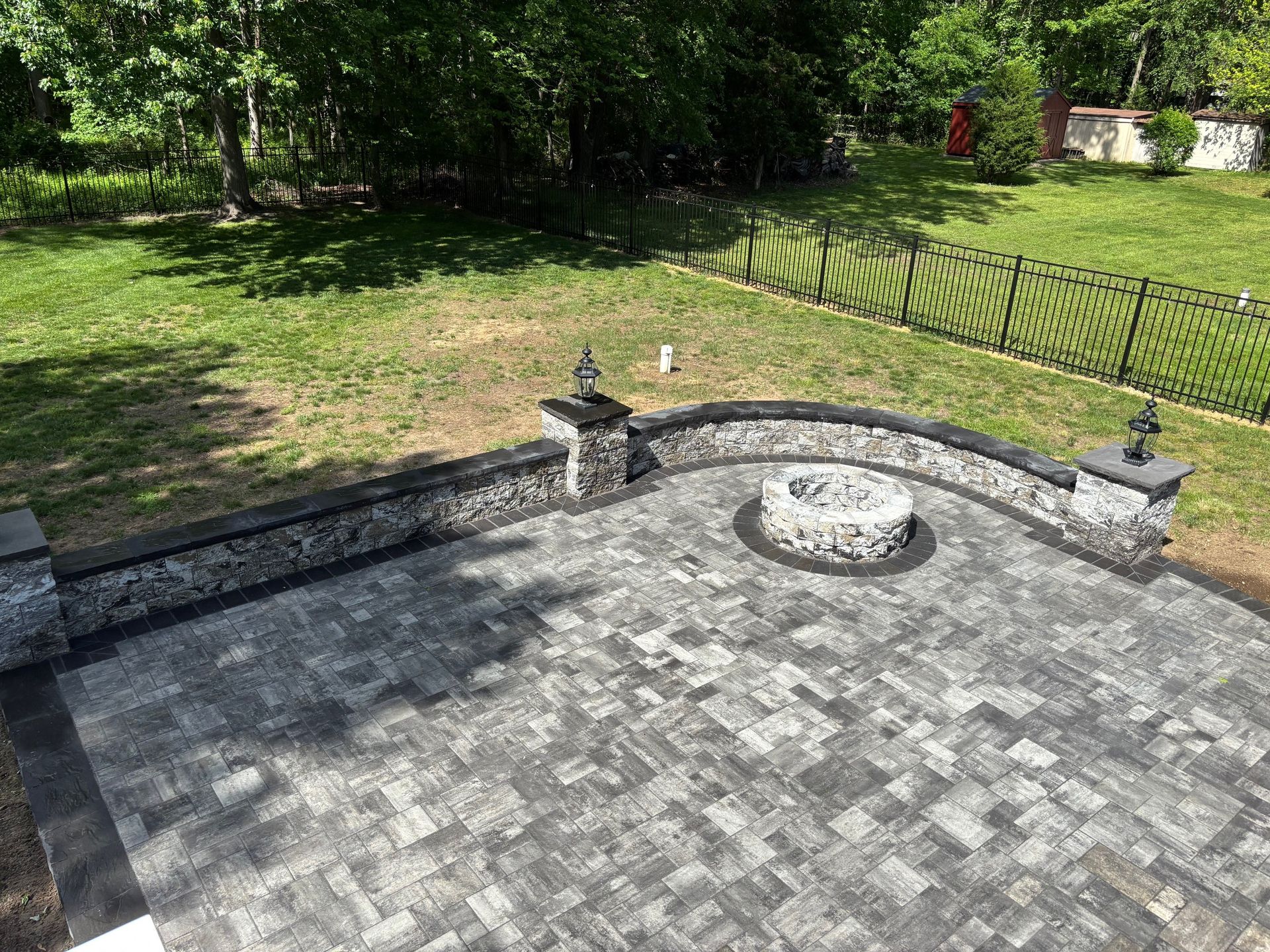 Stone patio with circular fire pit and low wall beside a grassy yard and trees