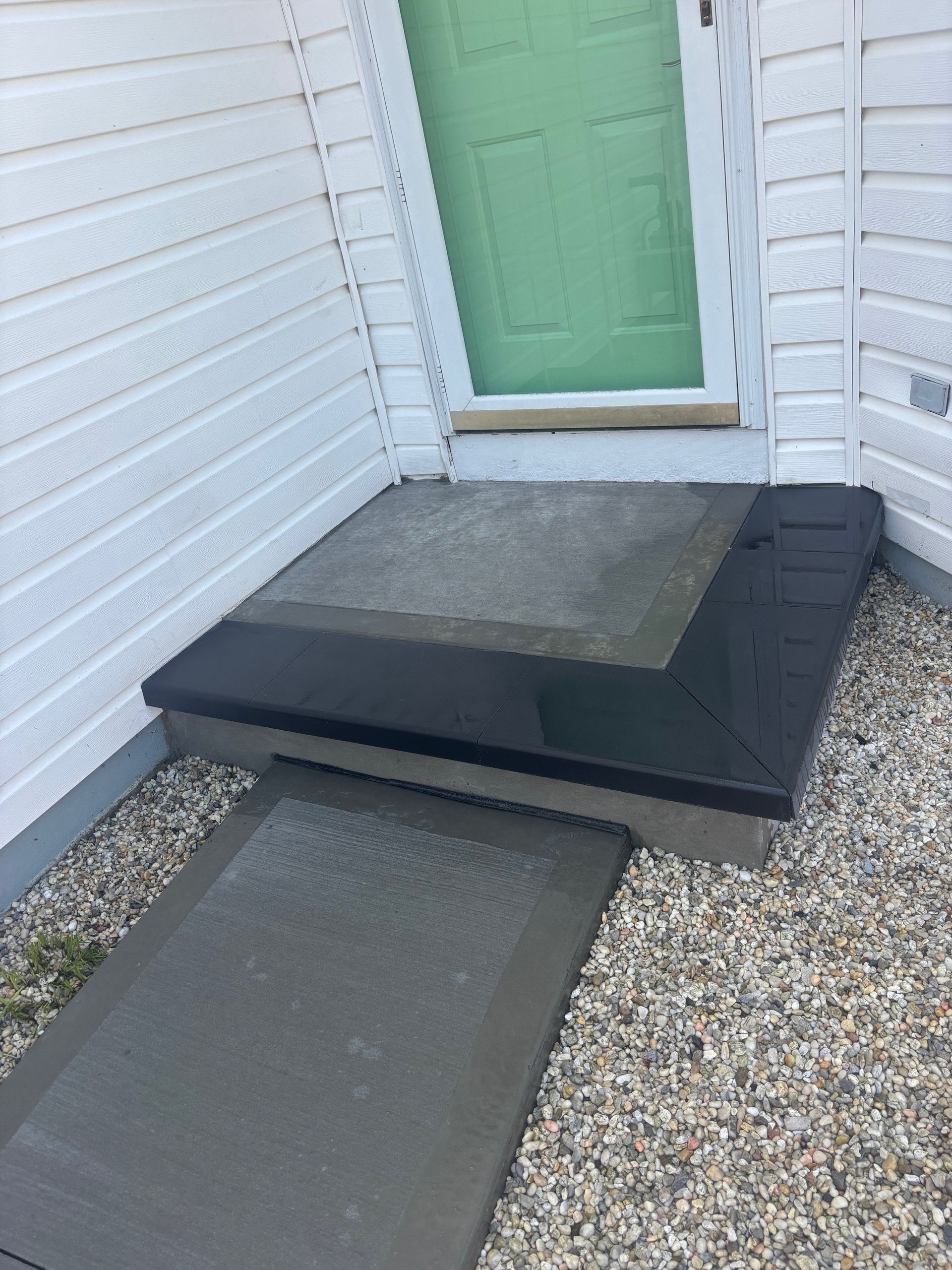 Front door with a portable black ramp and concrete step leading to a green entryway.