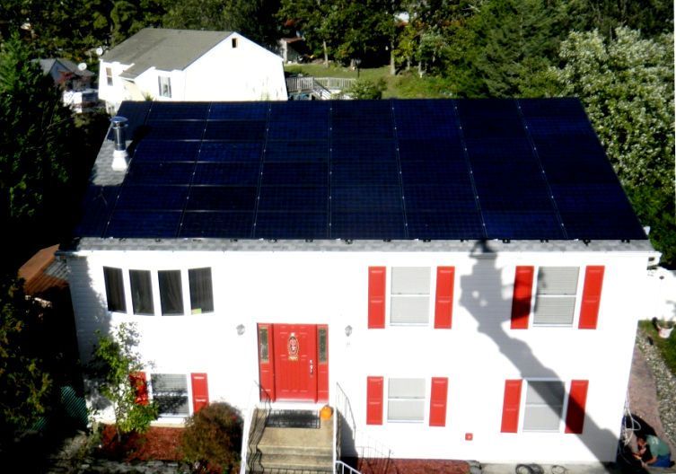 A white house with red shutters and solar panels on the roof.