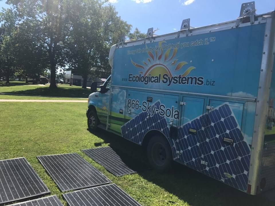 A van with solar panels on the side is parked in a grassy field.