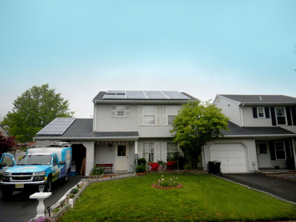 A blue truck is parked in front of a house with solar panels on the roof.