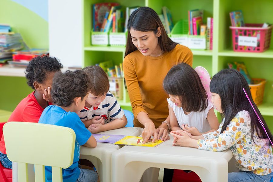 A group of children are sitting at a table with a teacher.