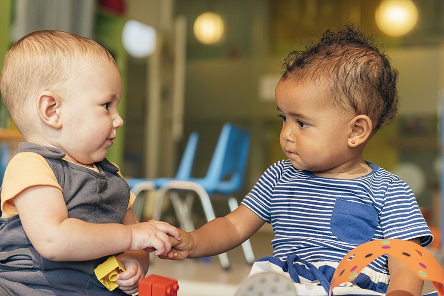 Two babies are holding hands and playing with toys in a room.