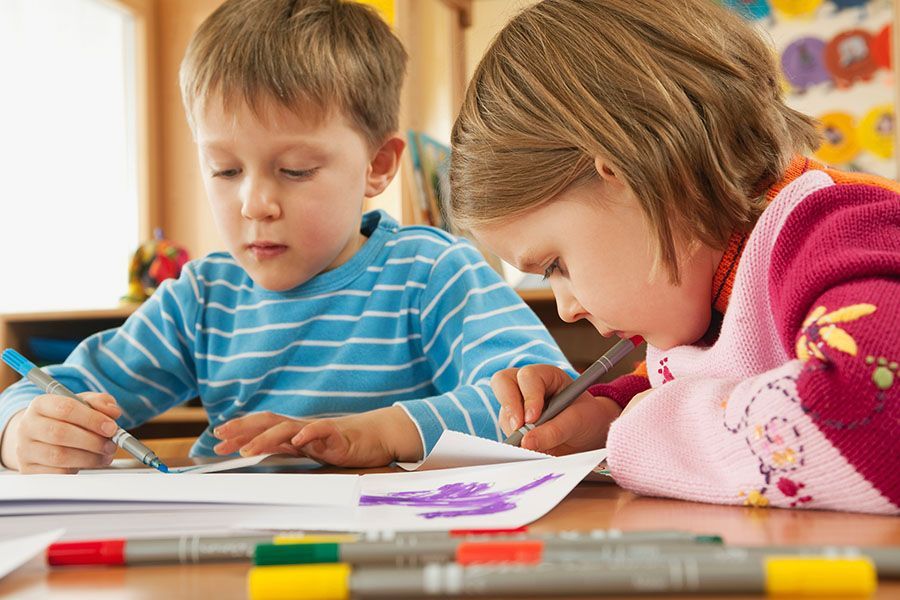 A boy and a girl are sitting at a table drawing with markers.