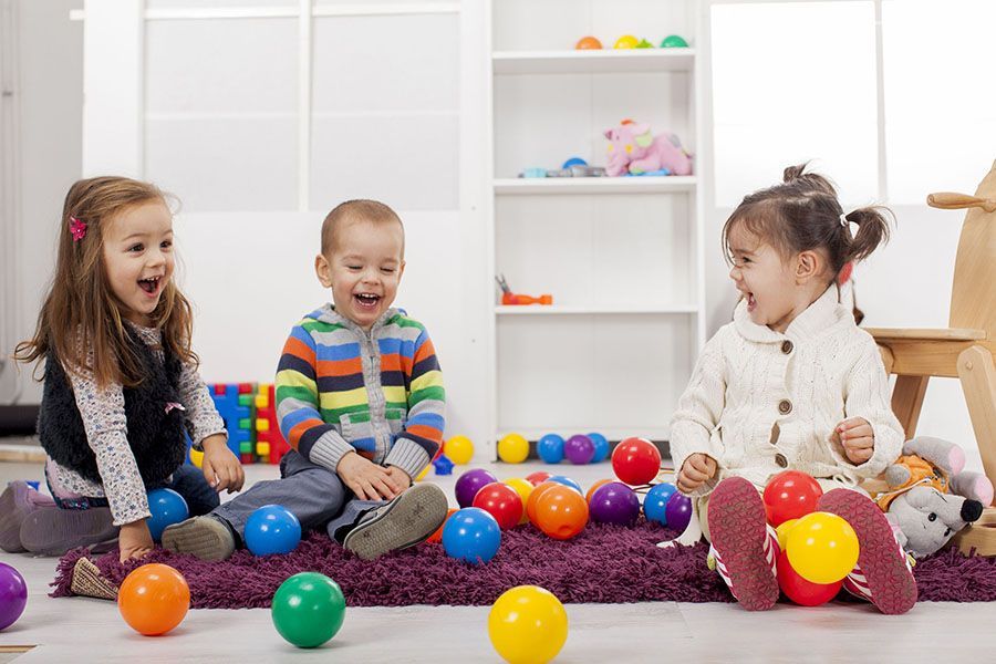 Three children are sitting on the floor playing with colorful balls.