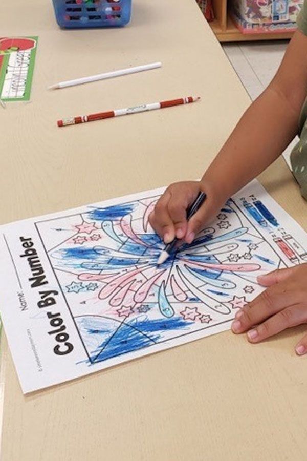 A child is drawing a fireworks display on a color by number sheet